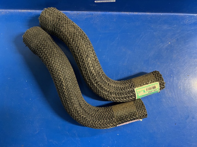 Braided black tow strap laid in a loose U-shape on a blue surface, with a green label on one end.