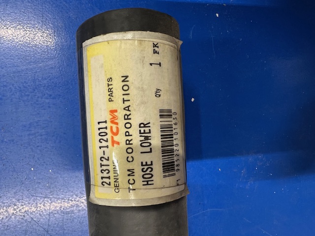 Close-up of a black automotive hose with a white label reading 'HOSE LOWER' and 'TCM CORPORATION'./close-up of a black automotive hose with a white label that says HOSE LOWER and TCM CORPORATION.