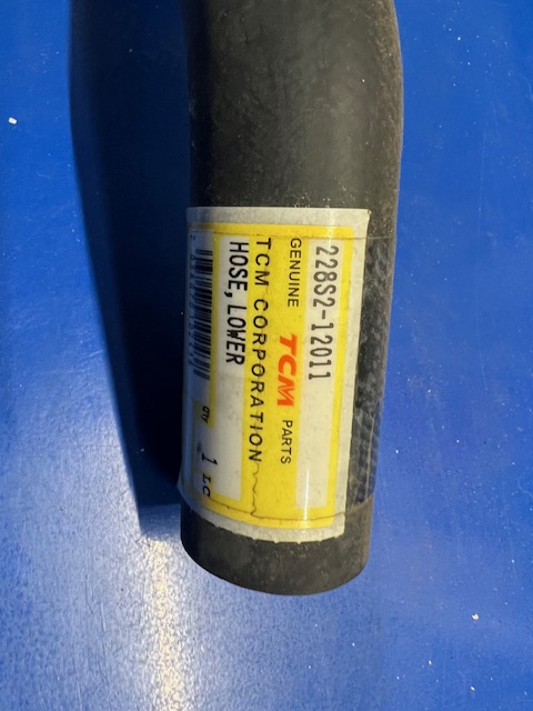 Black rubber hose with a yellow label that reads Genuine Parts, TCM Corporation, Hose_Lower, part number 228S-12011 (tubular object on blue surface).