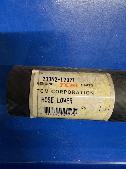 Hose labeled 'HOSE LOWER' from TCM Corporation, on a blue surface; part tag shows model 233N2-12021 and barcode.