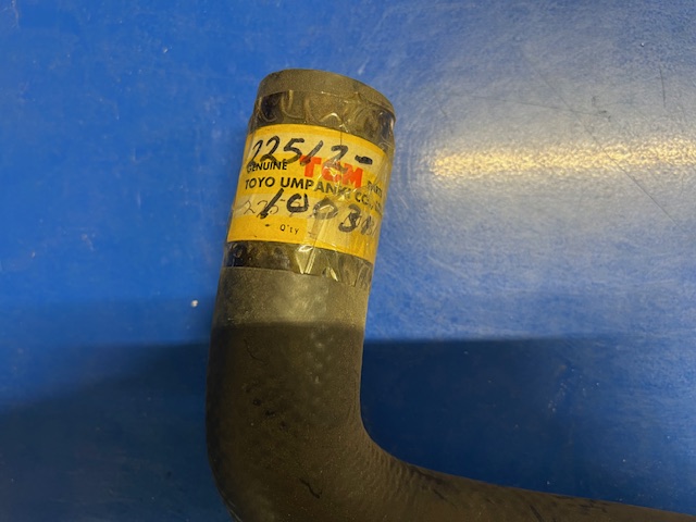 Black rubber engine hose elbow with a yellow tape label reading 'Genuine Toyota' on a blue surface.