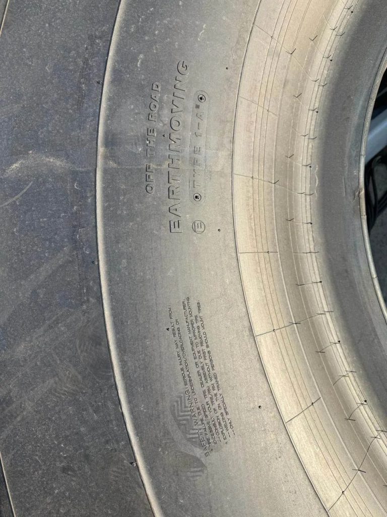Close-up of a tire sidewall showing the brand name 'EARTHMOTION' and warning text, with tread visible along the edge.