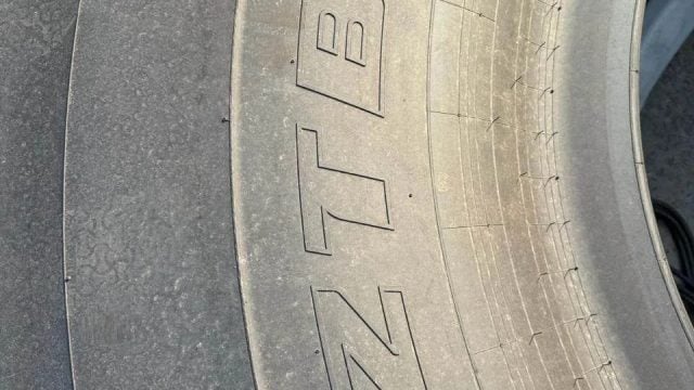 Close-up of a dusty tire sidewall with large raised lettering and visible tread along the edge.