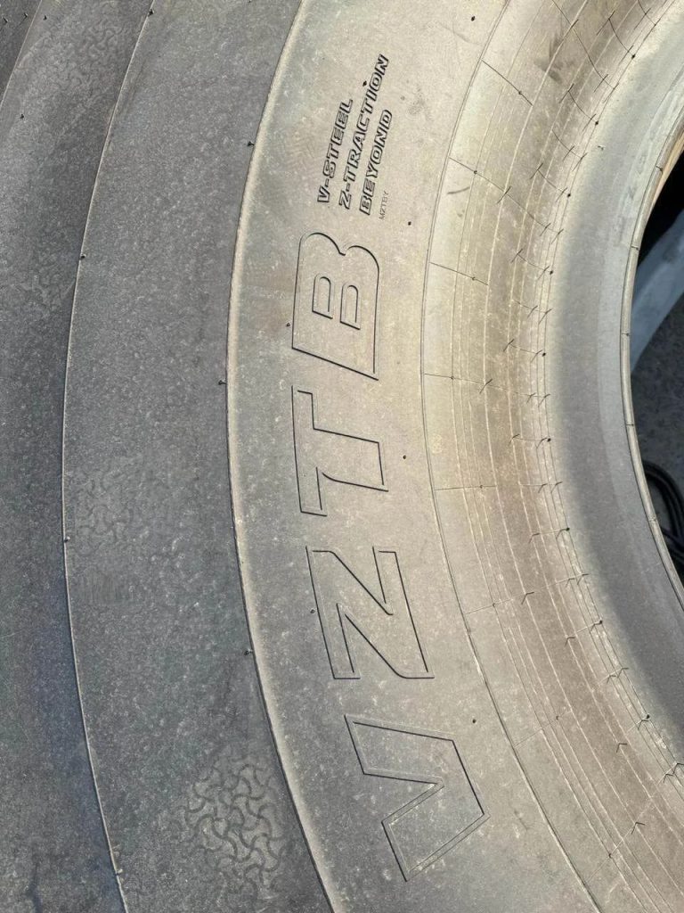 Close-up of a dusty tire sidewall with large raised lettering and visible tread along the edge.